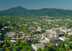 Aerial shot of Eugene, Oregon on a sunny day in summer, with the distinct shape of Spencer Butte in the distance.